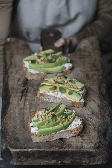 Woman holding chopping board, with ricotta, avocado and walnut bruschetta on top, close-up — Stock Photo
