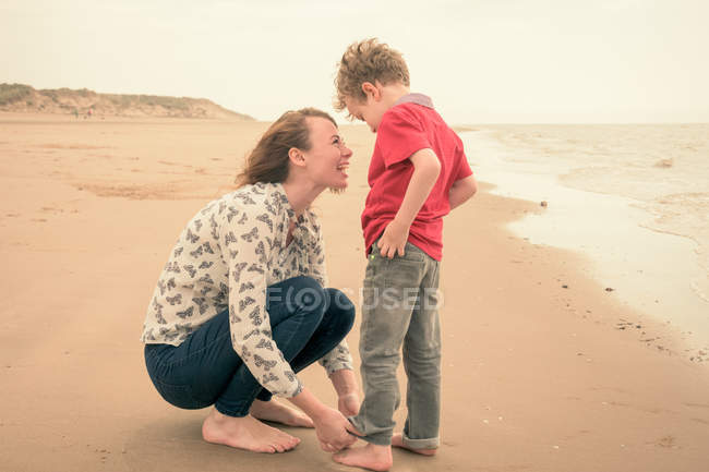 Junge Frau rollt Sohn Jeans am Strand auf — Stockfoto
