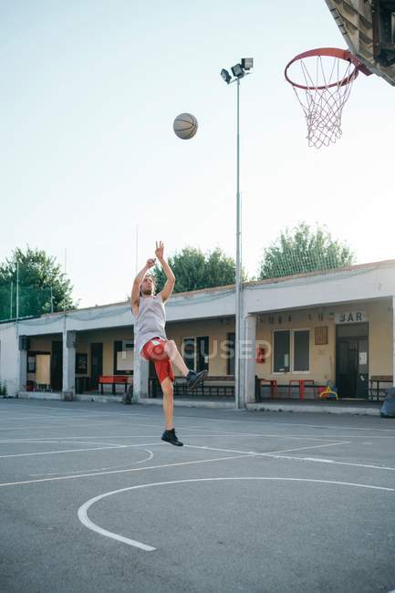 Hombre saltando al aro de baloncesto en el patio de recreo - foto de stock