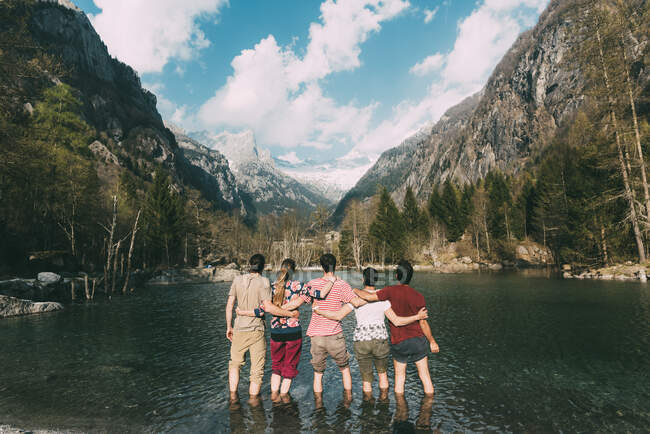 Vue arrière de cinq amis adultes cheville profondément dans le lac de montagne, Lombardie, Italie — Photo de stock