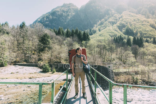 Молодой человек альпинист, стоящий на речном мосту — стоковое фото
