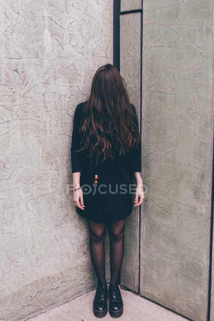 Portrait of young woman standing in corner, hair covering face — Stock Photo
