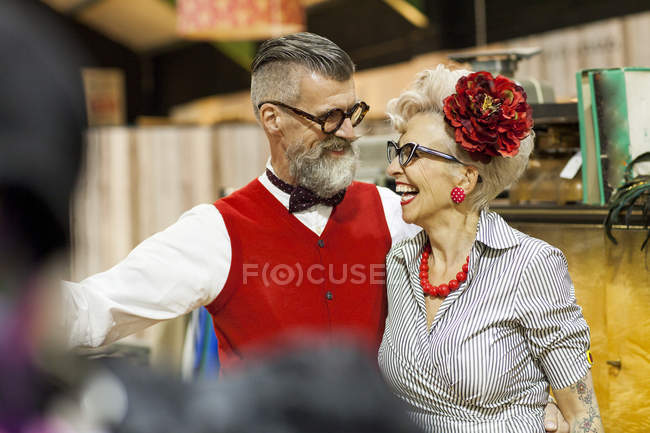 Quirky vintage couple laughing and looking at each other in antique emporium — Stock Photo