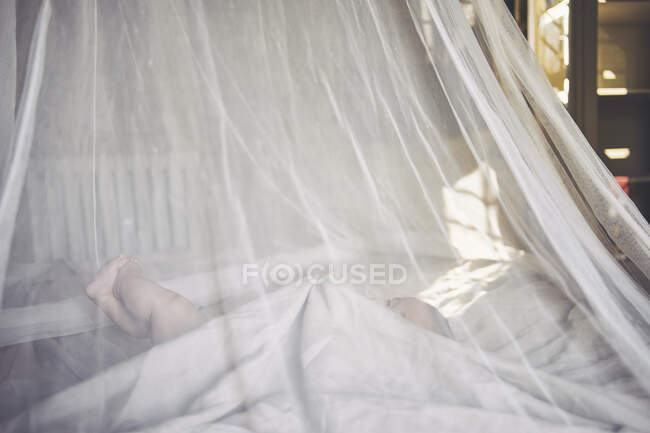 Девочка лежит в чистой драпированной кроватке, хватаясь за простыню. — стоковое фото