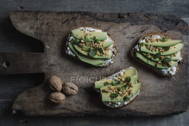 Натюрморт из рикотты, авокадо и брускетты из грецкого ореха на доске, вид сверху — стоковое фото