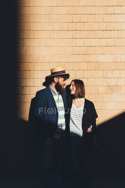 Cool coppia guardando l'un l'altro da parete di mattoni illuminata dal sole — Foto stock