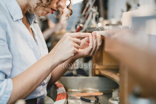 Female jeweler shaping silver metal at workbench — Stock Photo