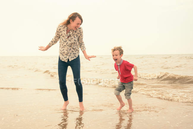 Молодая женщина и сын играют в море — стоковое фото