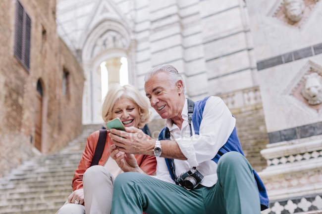 Pareja de turistas mirando el teléfono inteligente en la escalera de la catedral de Siena, Toscana, Italia - foto de stock
