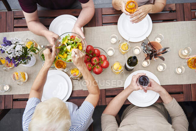 Overhead view of family handing salads at family lunch on patio — Stock Photo