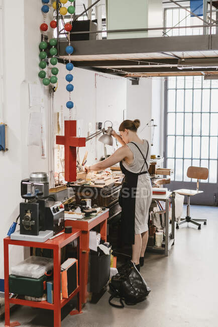 Female jeweller adjusting desk lamp at workbench — Stock Photo