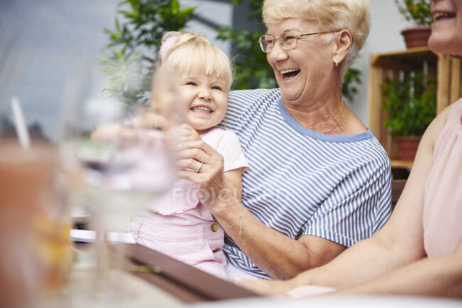 Senior woman laughing with toddler granddaughter at family lunch on patio — Stock Photo