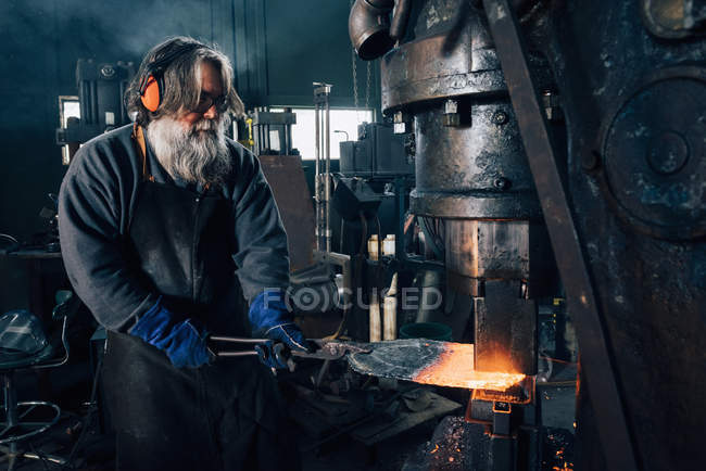 Blacksmith using blacksmith tongs for red hot metal in furnace — Stock Photo