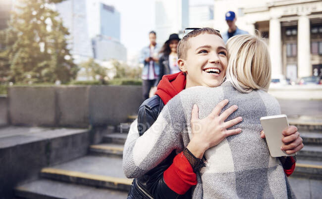 Dos amigas jóvenes abrazándose en la ciudad - foto de stock