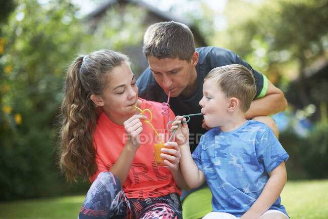 Uomo maturo con figlia adolescente e figlio che condividono frullato fresco in giardino — Foto stock