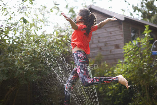 Ragazza che salta sopra irrigatore giardino — Foto stock