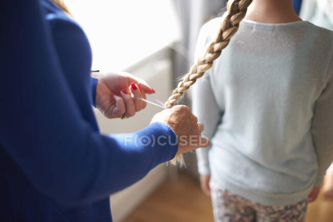 Cropped view of mother plaiting schoolgirl daughter's hair — Stock Photo