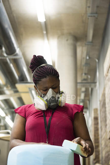 Woman in art studio wearing protective mask sanding object — Stock Photo