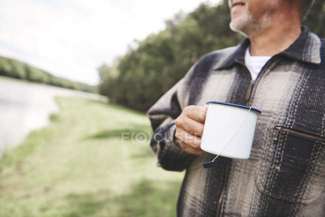 Senior man holding tin cup in rural setting — Stock Photo
