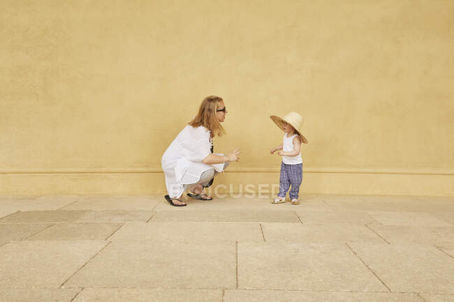 Mujer embarazada y su hija jugando por la pared amarilla - foto de stock