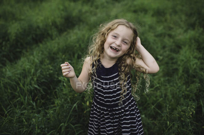 Menina olhando para a câmera no campo verde gramado — Fotografia de Stock