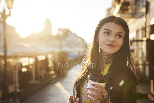 Mujer joven al aire libre, sosteniendo taza de café, tatuajes en las manos y el cuello - foto de stock