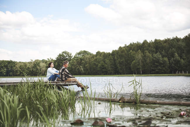 Зріла пара розслабляється на дерев'яному пірсі біля озера — стокове фото