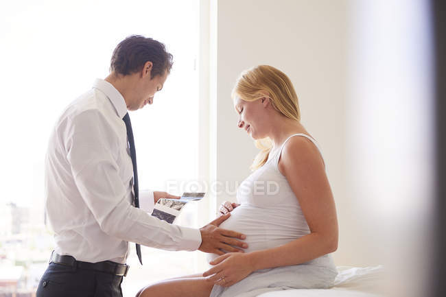 Vue latérale du couple enceinte regardant des images d'échographie — Photo de stock
