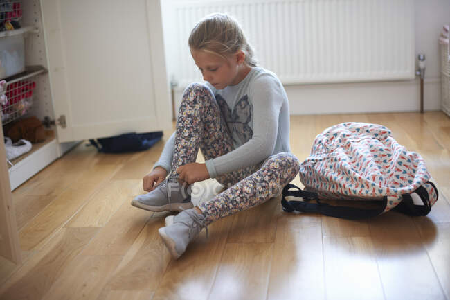 Menina sentada no chão do quarto amarrando espólio laços — Fotografia de Stock