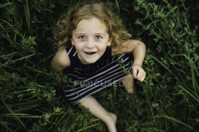 Chica mirando hacia arriba a la cámara en el campo de hierba verde - foto de stock