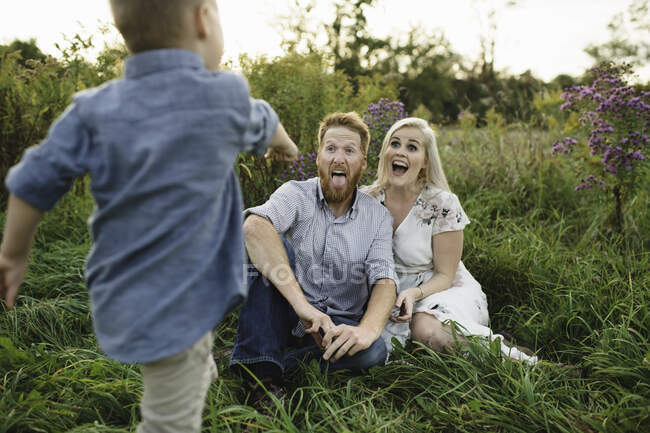 Boy surprising parents sitting in tall grass — Stock Photo