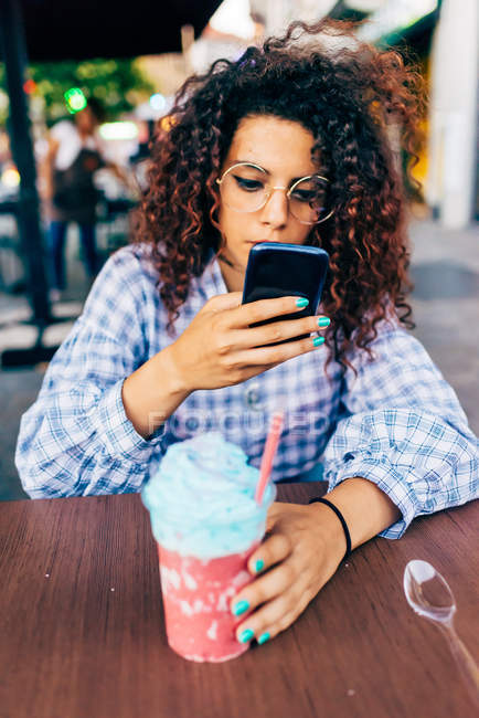 Жінка використовує мобільний телефон, насолоджуючись крижаним напоєм — стокове фото