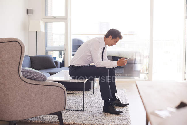 Geschäftsmann sitzt auf Couchtisch und schaut aufs Smartphone — Stockfoto