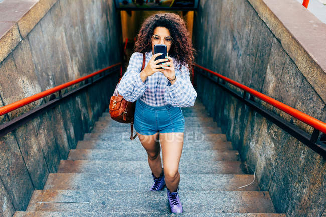 Femme montant les escaliers et utilisant un téléphone portable, Milan, Italie — Photo de stock