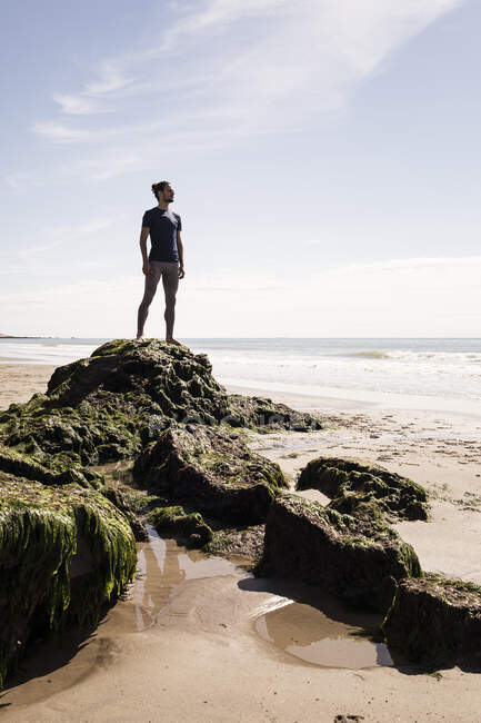 Young male runner looking out at sea from beach rock — Stock Photo