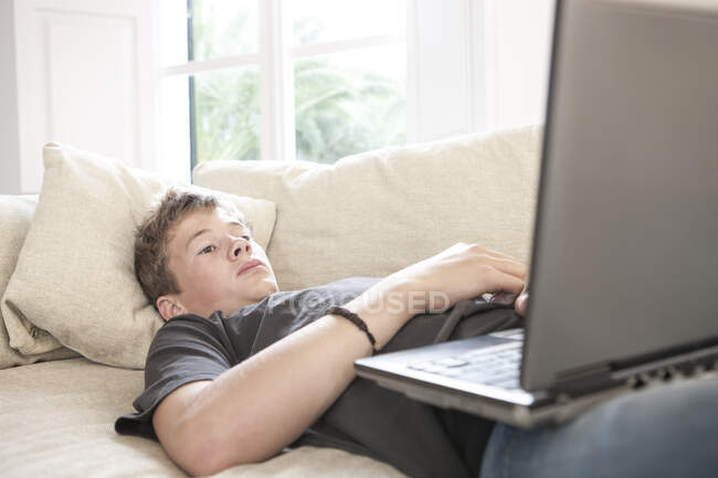 Teenager liegt auf Sofa und schaut auf Laptop — Stockfoto
