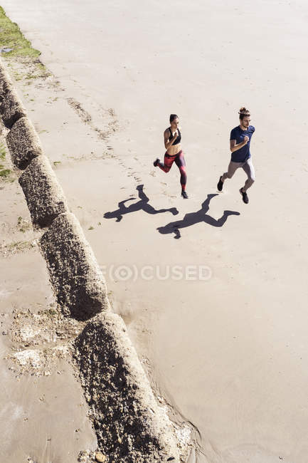 Joven hombre y mujer corriendo por la playa - foto de stock