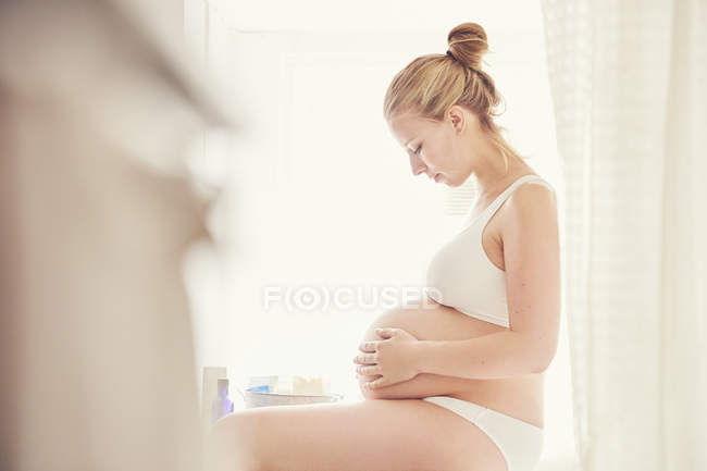 Vista lateral de la mujer embarazada abrazando el vientre - foto de stock