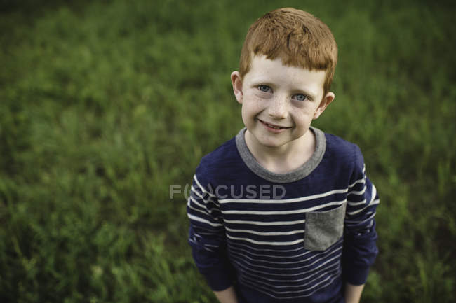 Портрет рыжего мальчика, стоящего на траве — стоковое фото