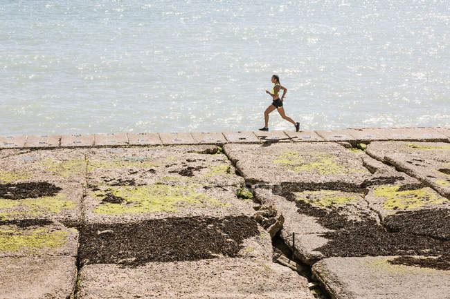 Young woman running along sea wall — Stock Photo