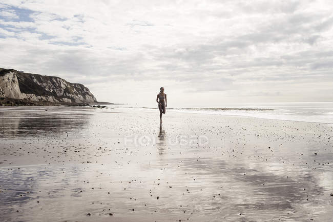 Giovane donna che corre lungo la spiaggia — Foto stock
