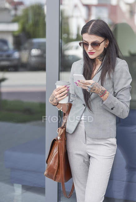 Femme d'affaires avec tasse à café en utilisant un smartphone — Photo de stock