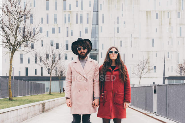 Portrait of young couple in urban setting, wearing sunglasses, holding hands — Stock Photo