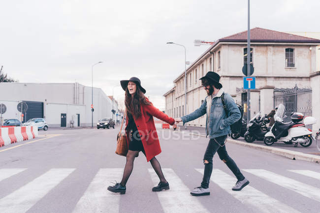 Young couple crossing road, holding hands, laughing — Stock Photo