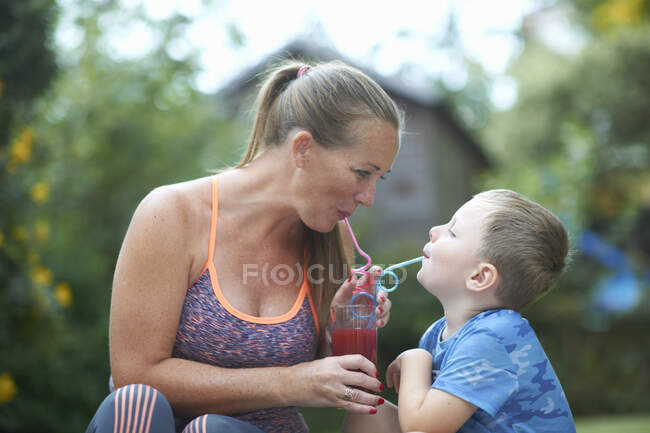 Menino e mãe compartilhando smoothie fresco no jardim — Fotografia de Stock