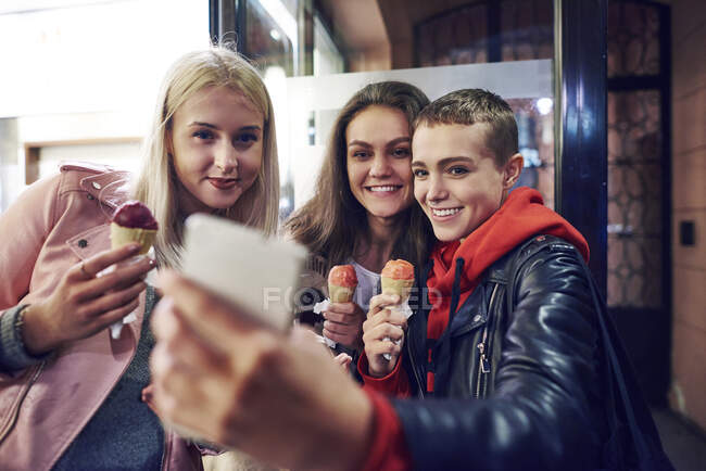 Três jovens mulheres com cones de sorvete levando selfie smartphone na rua da cidade — Fotografia de Stock