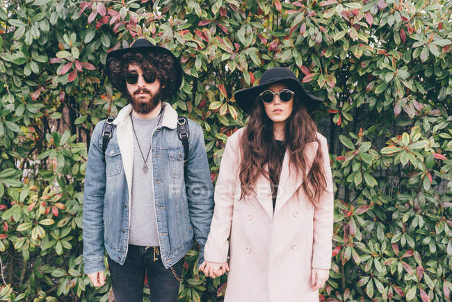 Porträt eines jungen Paares, das Hüte und Sonnenbrillen trägt und Händchen hält — Stockfoto