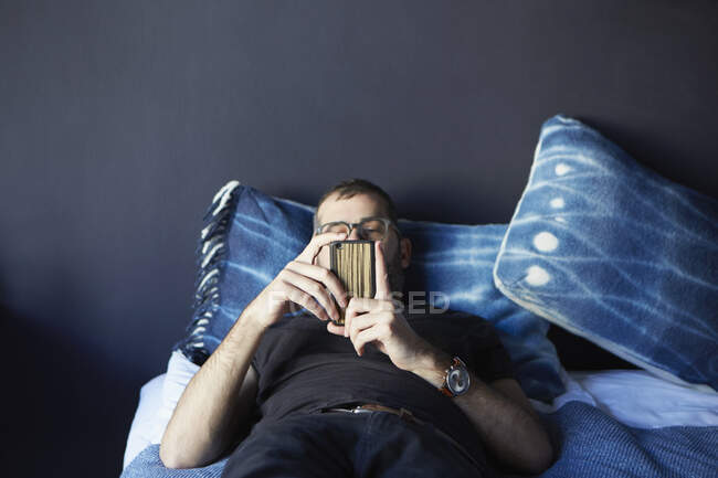 Молодий чоловік лежить на ліжку, дивлячись на смартфон — стокове фото