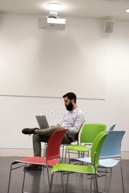 Человек сидит на стуле в офисе с помощью ноутбука — стоковое фото