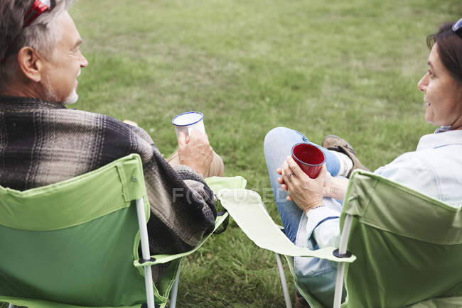Coppia matura seduta su sedie da campeggio, con coppe di latta in mano, vista posteriore — Foto stock